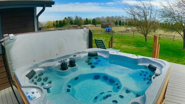 Een hottub op een houten terras, met uitzicht op een gazon en bomen.