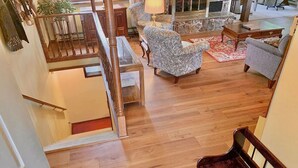 Een ruime woonkamer met een houten trap, een gestreept fauteuil en een lamp.