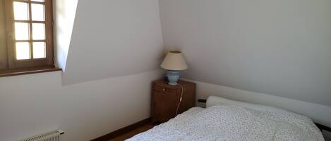 Ein Schlafzimmer mit Bett, Nachttisch mit Lampe, Heizkörper und Fenster.