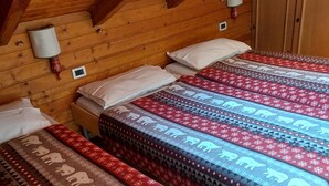Ein gemütliches Cabin-Zimmer mit Holzwänden und einer geneigten Decke. Es gibt drei Betten mit gemusterten Betttextilien und eine kleine Wandleuchte.