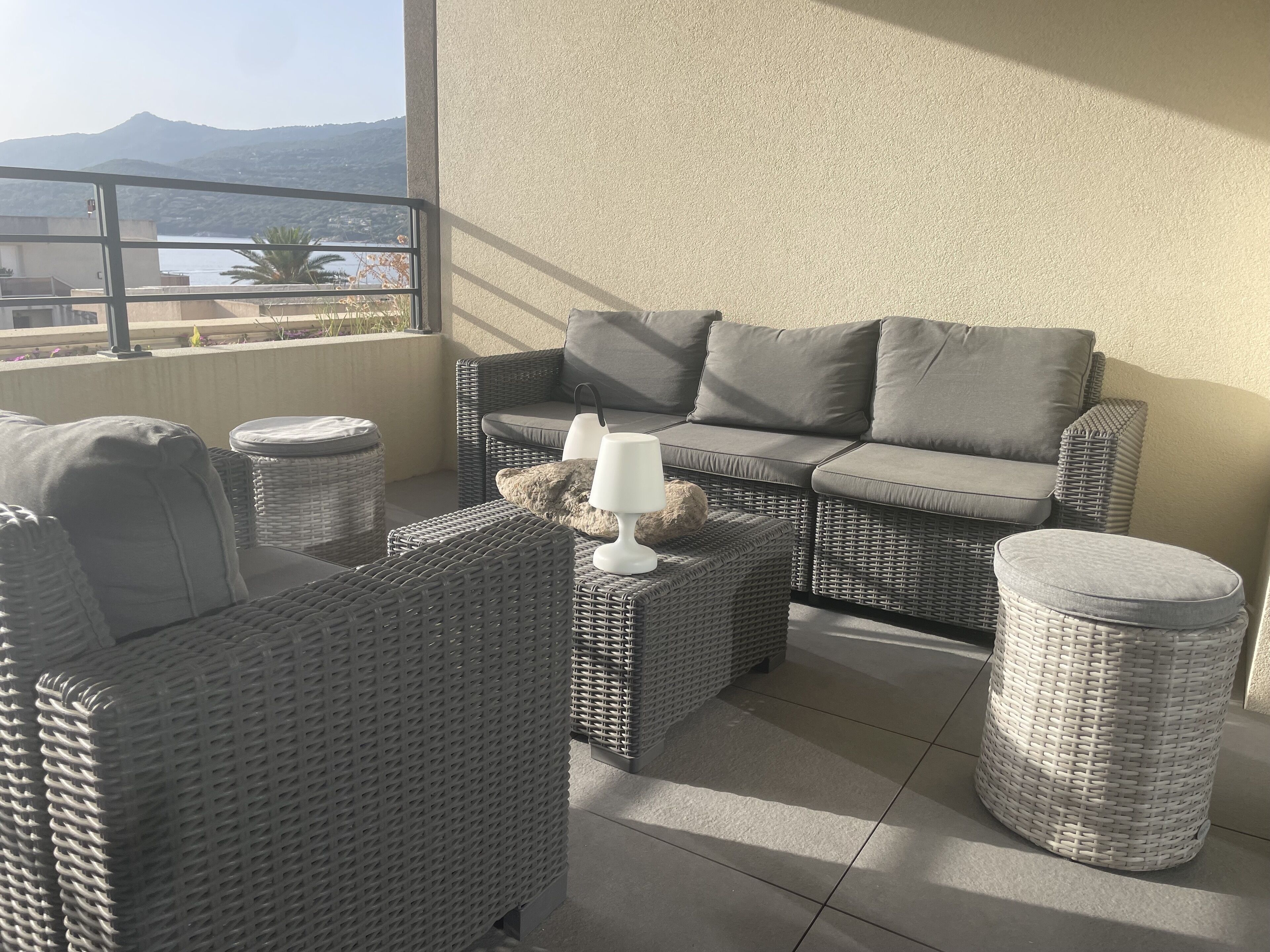 A balcony with wicker furniture, including a sofa and chairs, and a small table with a lamp.