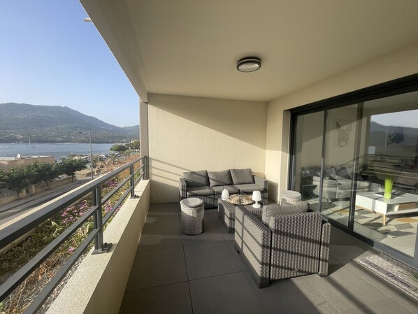 A balcony with wicker furniture, a glass door, and a view of the sea and mountains.