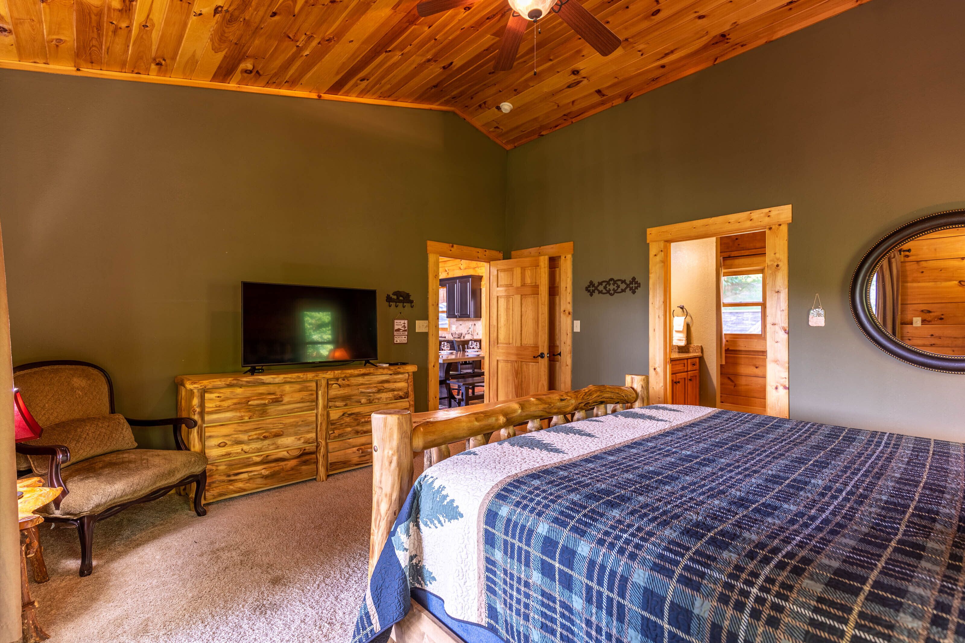 Une chambre avec un plafond en bois, un lit recouvert d’une couvre-lit à motifs bleus et blancs, une commode en bois, un téléviseur et une chaise.
