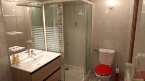 Ett modernt badrum med en duschavdelning med glasväggar, en vit tvättställsskål och ett träfärgat handfat samt en röd toalett.