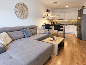 A modern living room with a grey sectional sofa, a wooden coffee table, and a large wall clock. - E2 Luxury OldTown Apt~2xFree Parking~Supermarket~PCScreen~Crib~Aircon~FastWifi (Košický kraj)