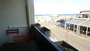 En balkong med utsikt över en strand, en restaurang som heter ”GLACES” och parkerade bilar.