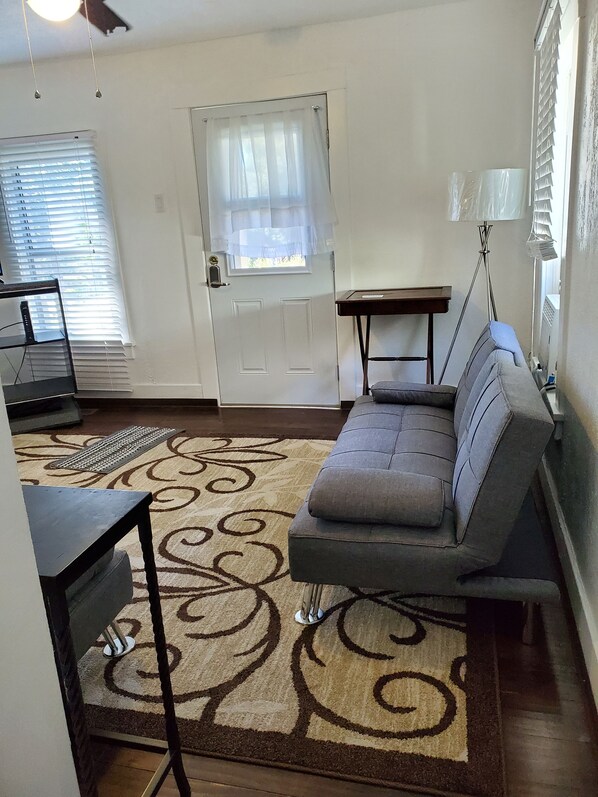 A living room with a sofa, a small table, a lamp, and a door with a window.