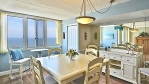 A dining area with a large table, chairs, and a hanging light fixture.