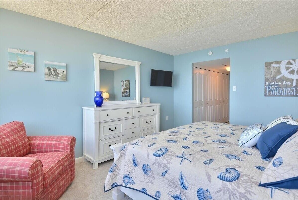 A bedroom with a bed, a dresser, a chair, and a TV.