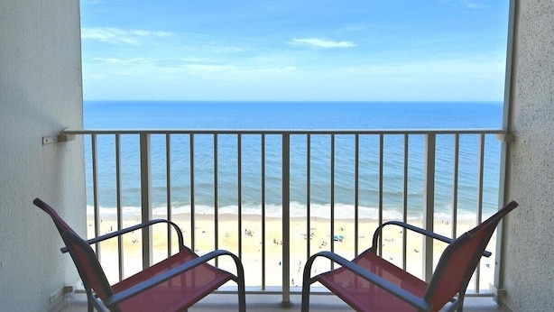 A balcony with two chairs facing a beach and the ocean.
