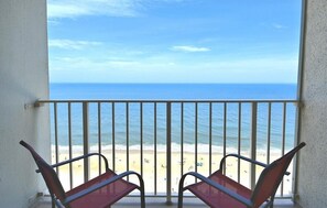 Un balcon avec deux chaises donnant sur une plage et l’océan.