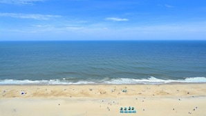 A beach with a clear sky, calm sea, and people walking along the shore.