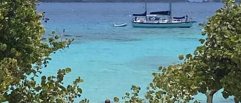 A beach with clear turquoise water, a sailboat, and distant mountains.