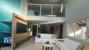 Ein modernes Wohnzimmer mit an der Holzwand montiertem Fernseher, einer Sofagarnitur, einem Couchtisch und einer Treppe, die zu einer oberen Ebene führt.