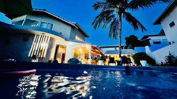 Ein modernes Haus mit Swimmingpool, Palme und Mond am Himmel.