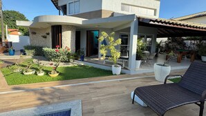 Ein modernes, zweistöckiges Haus mit überdachter Terrasse, Schwimmbecken und verschiedenen Kübelpflanzen.