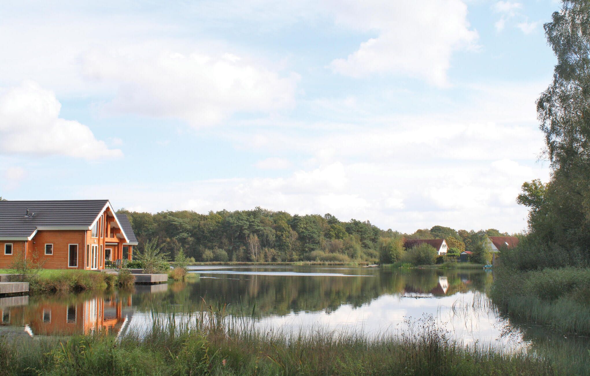A lakeside property with a wooden house, a dock, and a calm lake reflecting the sky.