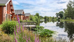 En vacker utsikt över floden med en träbrygga, en rad röda tegelhus och frodig grönska.
