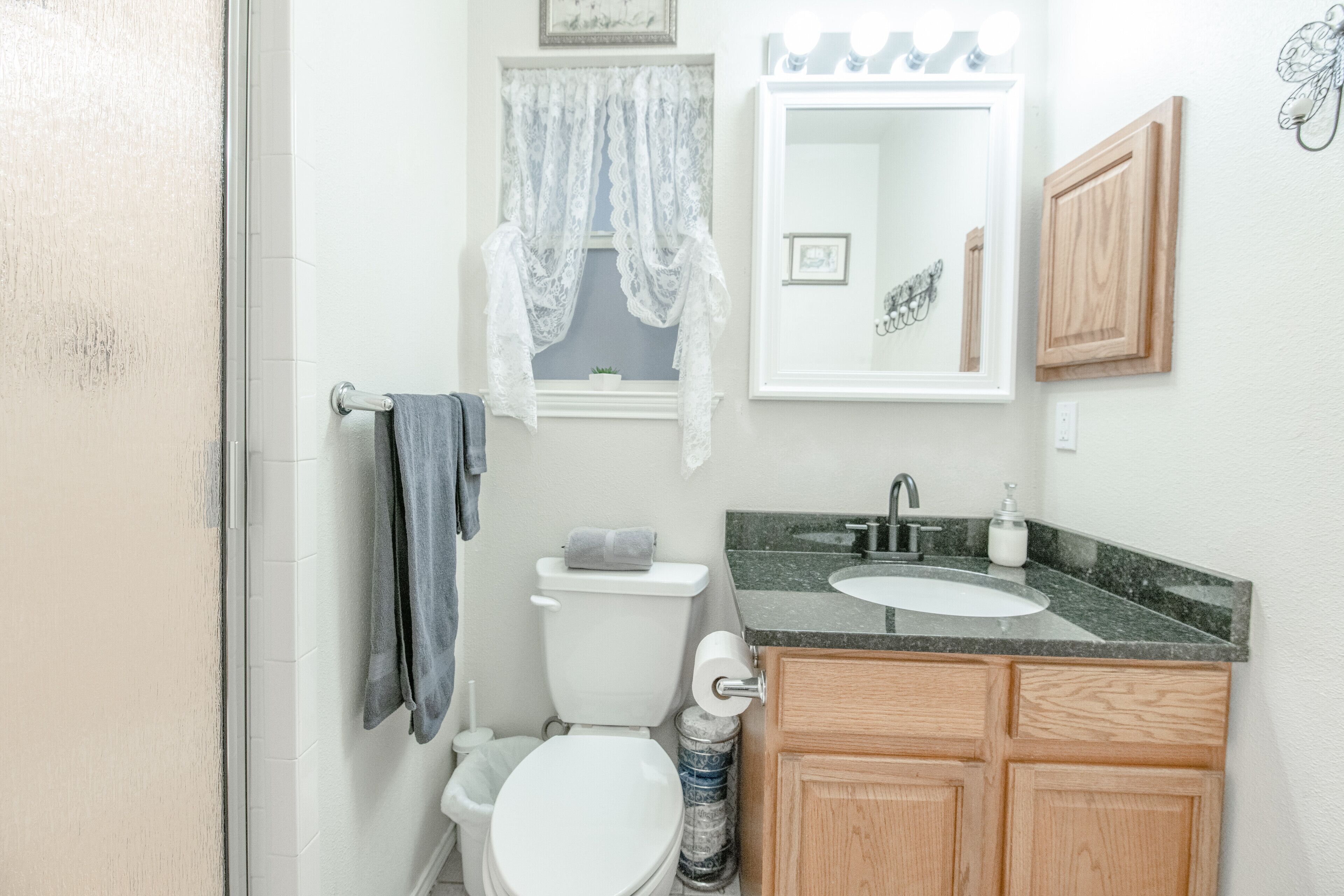A bathroom with a toilet, sink, vanity, and a window with lace curtains.