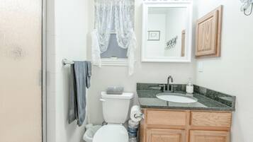 A bathroom with a toilet, sink, vanity, and a window with lace curtains.