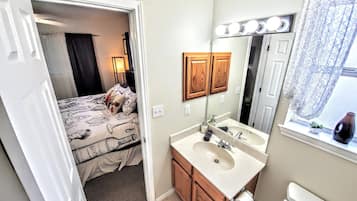 Une salle de bain avec un lavabo, un miroir et une petite fenêtre avec un rideau.