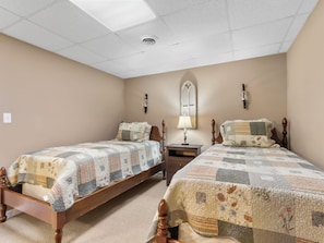Une chambre à coucher avec deux lits en bois, une table de chevet, une lampe fixée au mur et un luminaire au plafond.