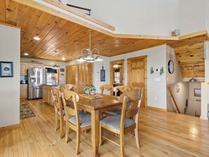 A wooden interior with a dining table, chairs, a refrigerator, and a kitchen area. - September Special | Hot Tub+Breathtaking Mtn Views (Spruce Pine)