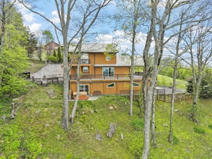 A multi-story wooden cabin with a balcony, surrounded by trees and a grassy area. - September Special | Hot Tub+Breathtaking Mtn Views (Spruce Pine)