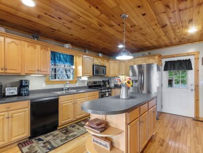 A kitchen with wooden cabinets, a stainless steel refrigerator, a coffee maker, and a vase with flowers on the counter. - September Special | Hot Tub+Breathtaking Mtn Views (Spruce Pine)