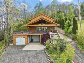 A two-story log cabin with a covered porch, a garage, and a landscaped yard. - September Special | Hot Tub+Breathtaking Mtn Views (Spruce Pine)
