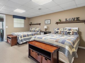A bedroom with two beds, a wooden bench, a small table, and a wall-mounted shelf with a sign.