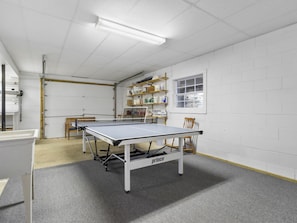 Une table de ping-pong dans une pièce aux murs blancs, avec une fenêtre et des étagères remplies de divers objets.