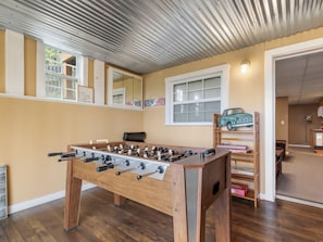 A room with a foosball table, a window with blinds, a shelf with toys, and a door leading to another room. - September Special | Hot Tub+Breathtaking Mtn Views (Spruce Pine)