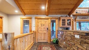 A wooden cabin interior with a central door, a stone wall, and a wooden railing. - Timberline Trail. Views, Hot Tub & Game Room (Big Bear Lake)