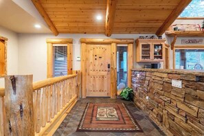 A wooden cabin interior with a central door, a stone wall, and a wooden railing. - Timberline Trail. Beautiful Views plus game room. (Big Bear Lake)