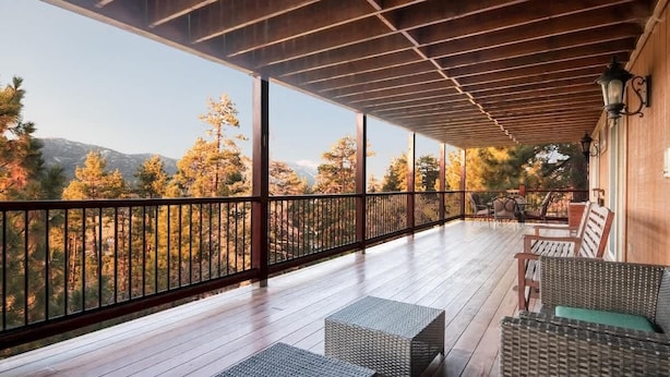 A covered outdoor deck with wicker furniture and a view of trees and mountains. - Timberline Trail. Views, Hot Tub & Game Room (Big Bear Lake)