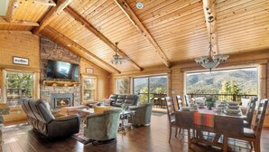 A spacious living area with a fireplace, comfortable seating, a dining table, and a large TV. - Timberline Trail. Views, Hot Tub & Game Room (Big Bear Lake)