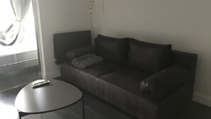 A modern living room with a dark brown leather sofa, a small round table, and a flat-screen TV mounted on the wall. - T2 Golf de Valescure, swimming pool, tennis court and private garden  (Saint-Raphaël)
