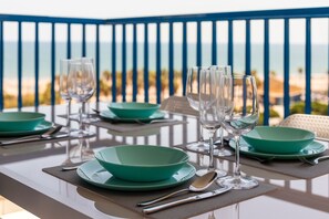 A table set with green plates, wine glasses, and cutlery on a balcony overlooking a beach. - Patacona Essense . WiFi + PK + A/ Conditioning + Pool (Alboraya)