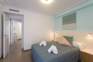 A hotel room with a bed, a bedside table, a nightstand, a wall-mounted light, and a door leading to a bathroom. - Patacona Essense . WiFi + PK + A/ Conditioning + Pool (Alboraya)