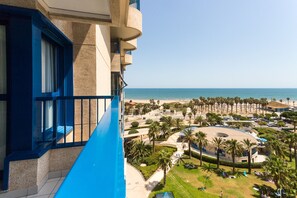 A high-rise hotel with a balcony overlooking a beach resort area, featuring palm trees, a pool, and a clear view of the ocean. - Patacona Essense . WiFi + PK + A/ Conditioning + Pool (Alboraya)
