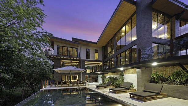 Una casa moderna de dos pisos con piscina, mobiliario exterior y ventanas grandes.