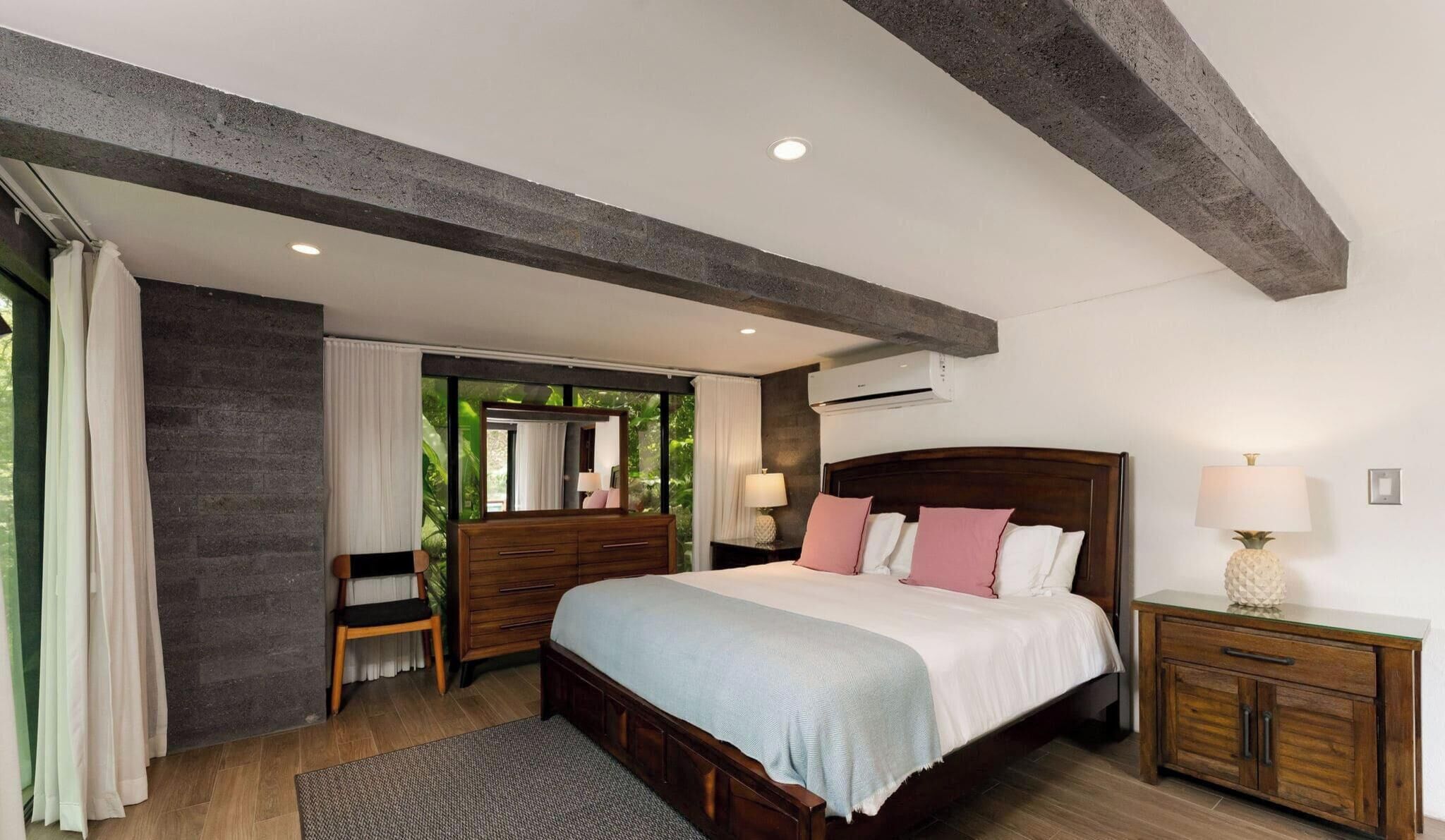 A bedroom with a wooden bed, a nightstand, a dresser, a chair, and a window with curtains.