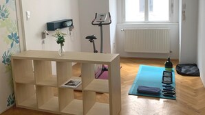 A room with a wooden floor, a standing desk, a yoga mat, a water bottle, and a bag.