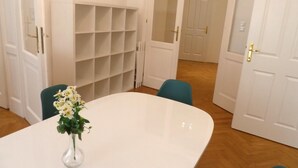 A room with a white table, teal chairs, a white shelving unit, and a white door.