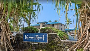 Skilt for Kona Reef med en stenvæg og tropisk vegetation.