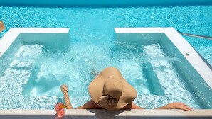 A pool with clear blue water, a person relaxing in a hot tub, and a view of the ocean and a road leading to a building. - Villa Hellena, Minimalist Design & Spa Retreat (Heraklion)
