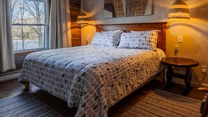 Een slaapkamer met een groot bed, een raam met gordijnen, een kamerkleed met dessin en een hanglamp.