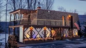 Een knus houten huisje met balkon, schoorsteen en kerstboom.