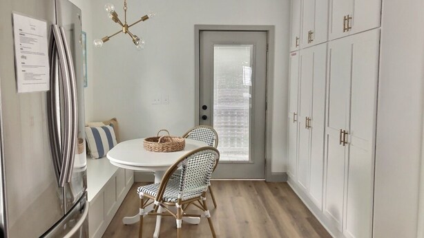 A compact kitchen with a white table, wicker chairs, a stainless steel refrigerator, and white cabinets. - Rock House - Lake Views & 15 Mins to Cedar Point (Huron)
